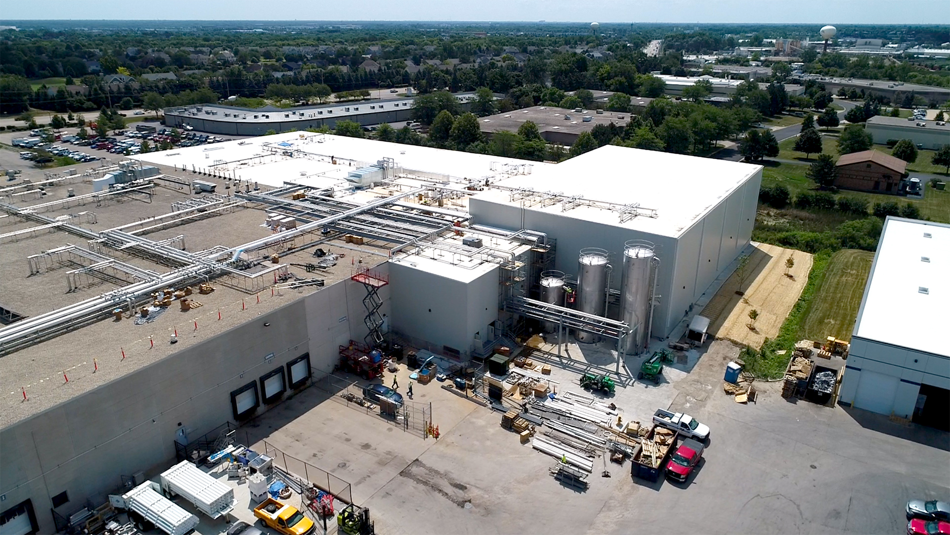 An aerial view of the massive Ruprecht Meat Company Processing Facility and surrounding parking lot. The building has white walls, pipes, metal grids, and exterior tanks on the roof and sides.