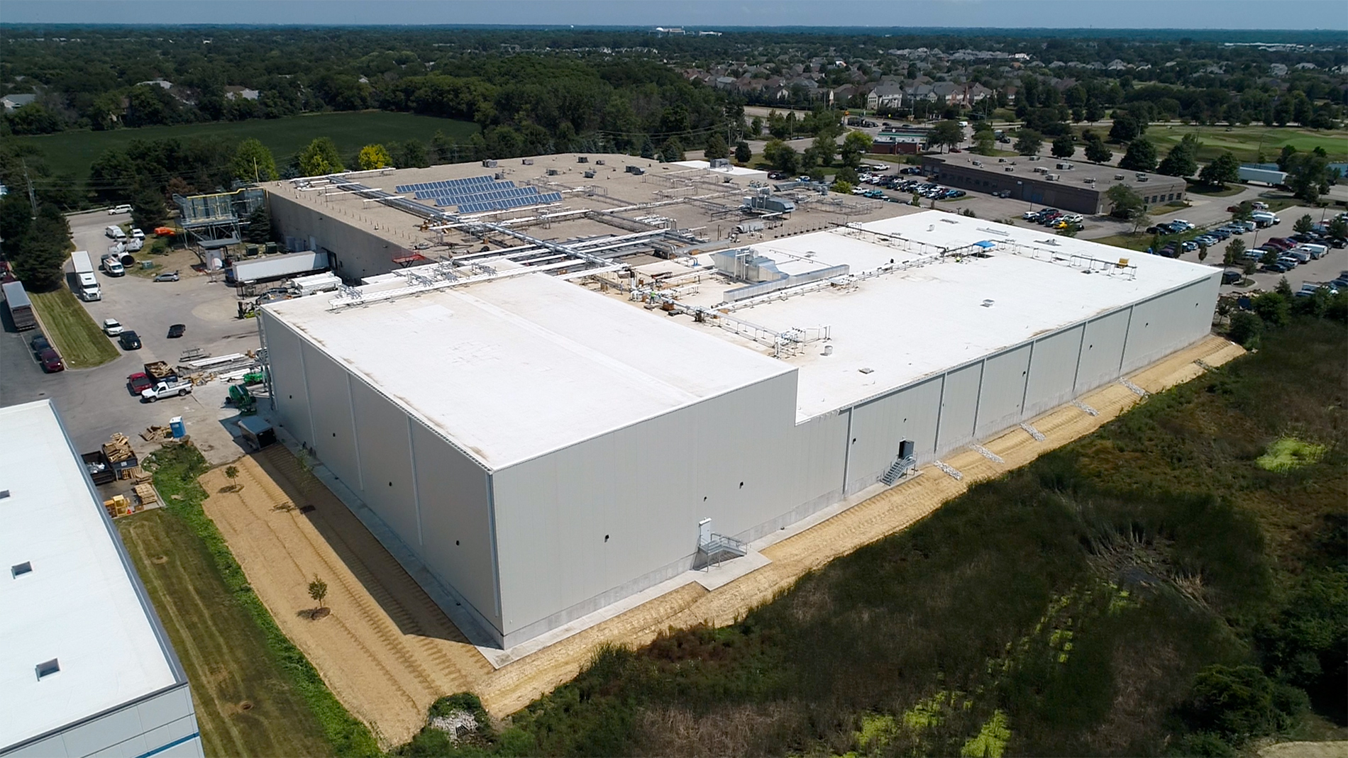 The back of the bright white Ruprecht Meat Company Processing Facility shows the massive size of the facility as well as newly sodded green areas, solar panels on the roof, and ongoing expansion construction done by Keeley Construction, Inc.