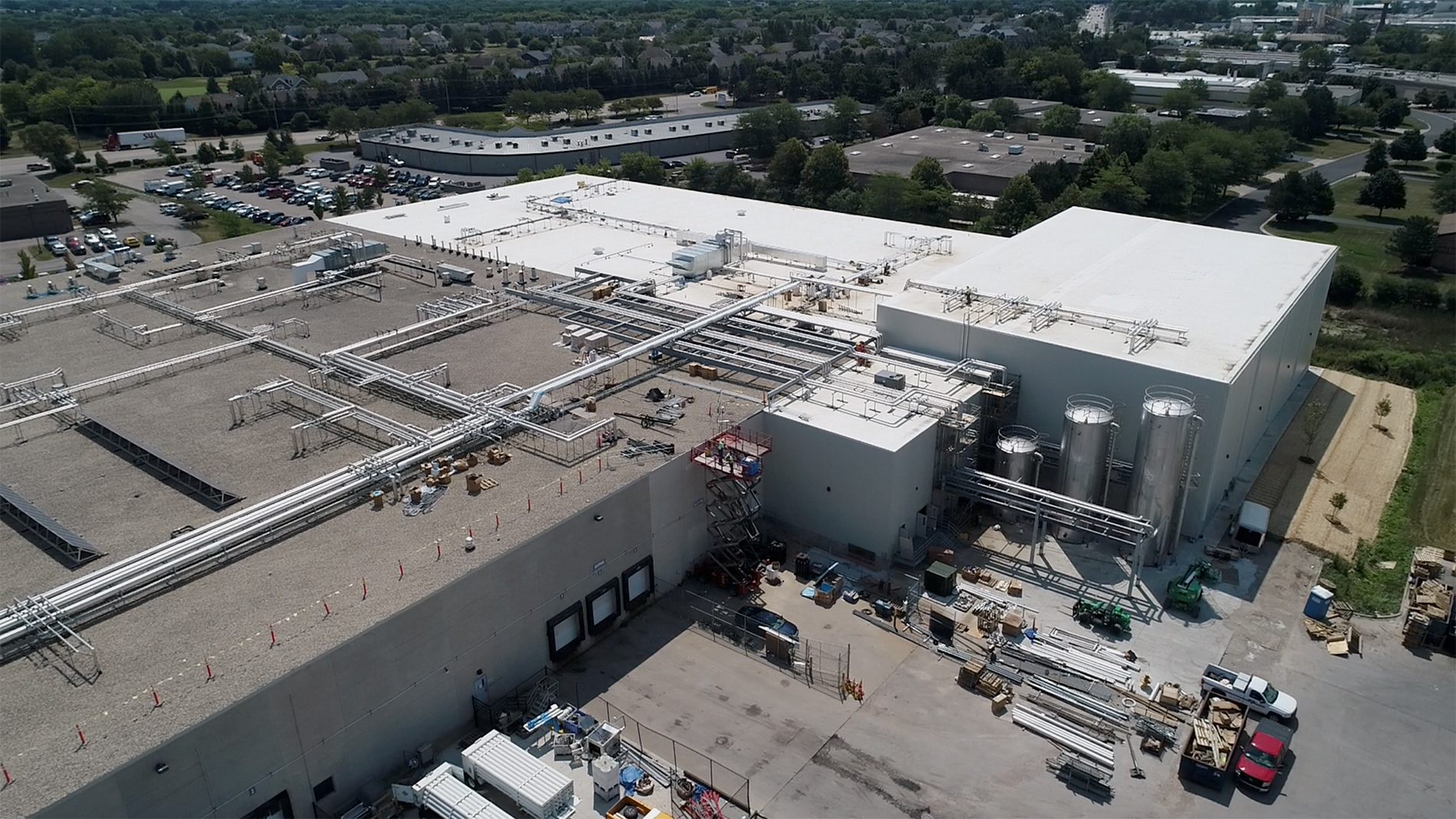 A bird’s eye view of the construction of the Ruprecht Meat Company Processing Facility expansion shows an elevator lift reaching the roof, metal grids, and pipes along the roof and sides of the building.