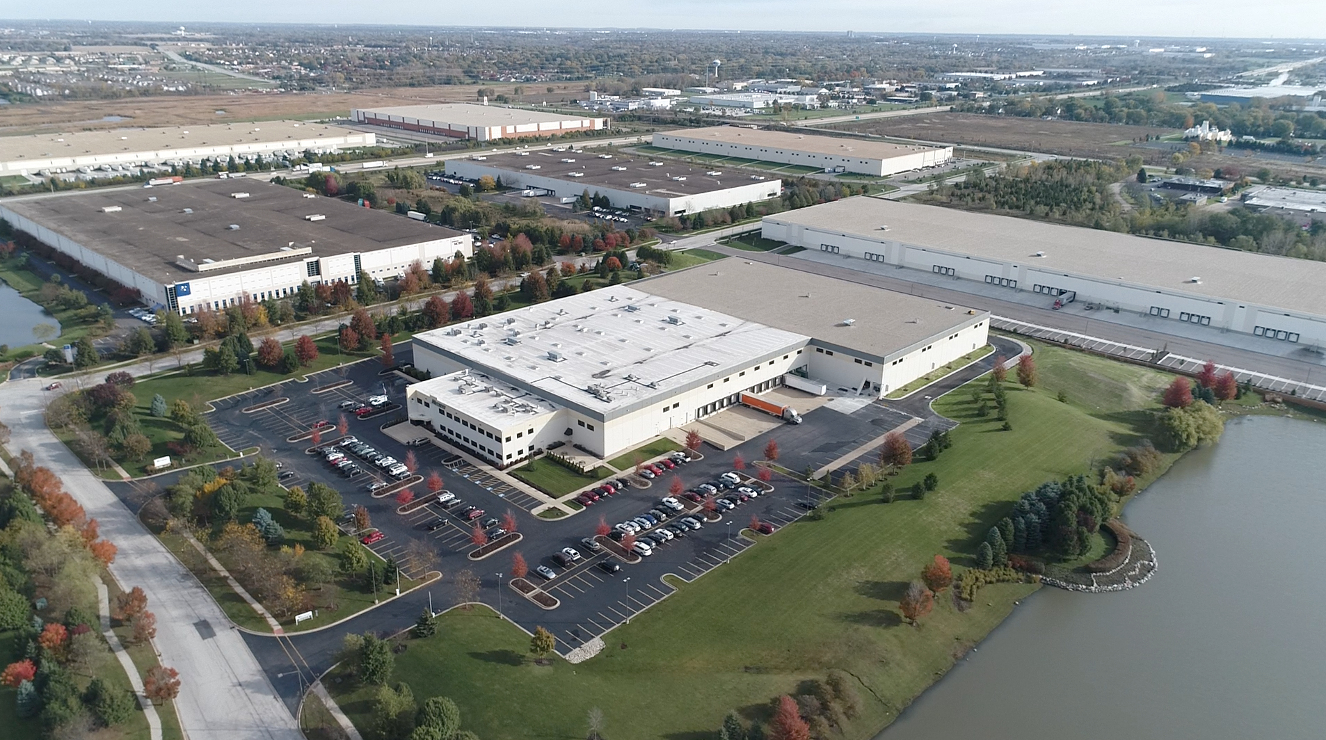 An aerial view of an industrial park with large buildings and a retention pond. The big center building is surrounded by a parking lot and manicured green spaces with trees turning red in the fall, and is the Nutrivo/Rule 1 Protein’s expansion, a new construction project by Keeley Construction, Inc.