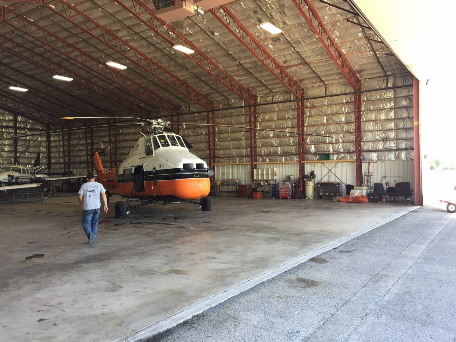 A man in jeans and a t-shirt walks toward a white and orange Midwest Helicopter in a large helicopter hangar built by Keeley Construction, Inc.