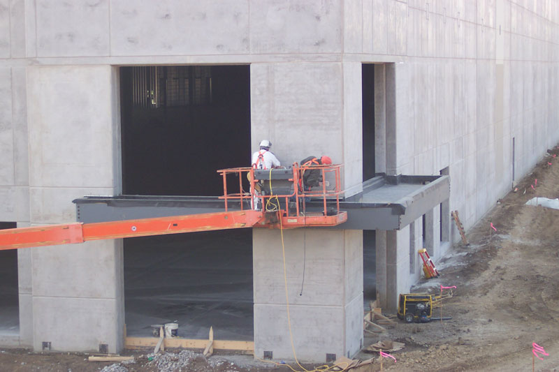 A Keeley Construction worker stands on a lift midway up a two-story concrete building.