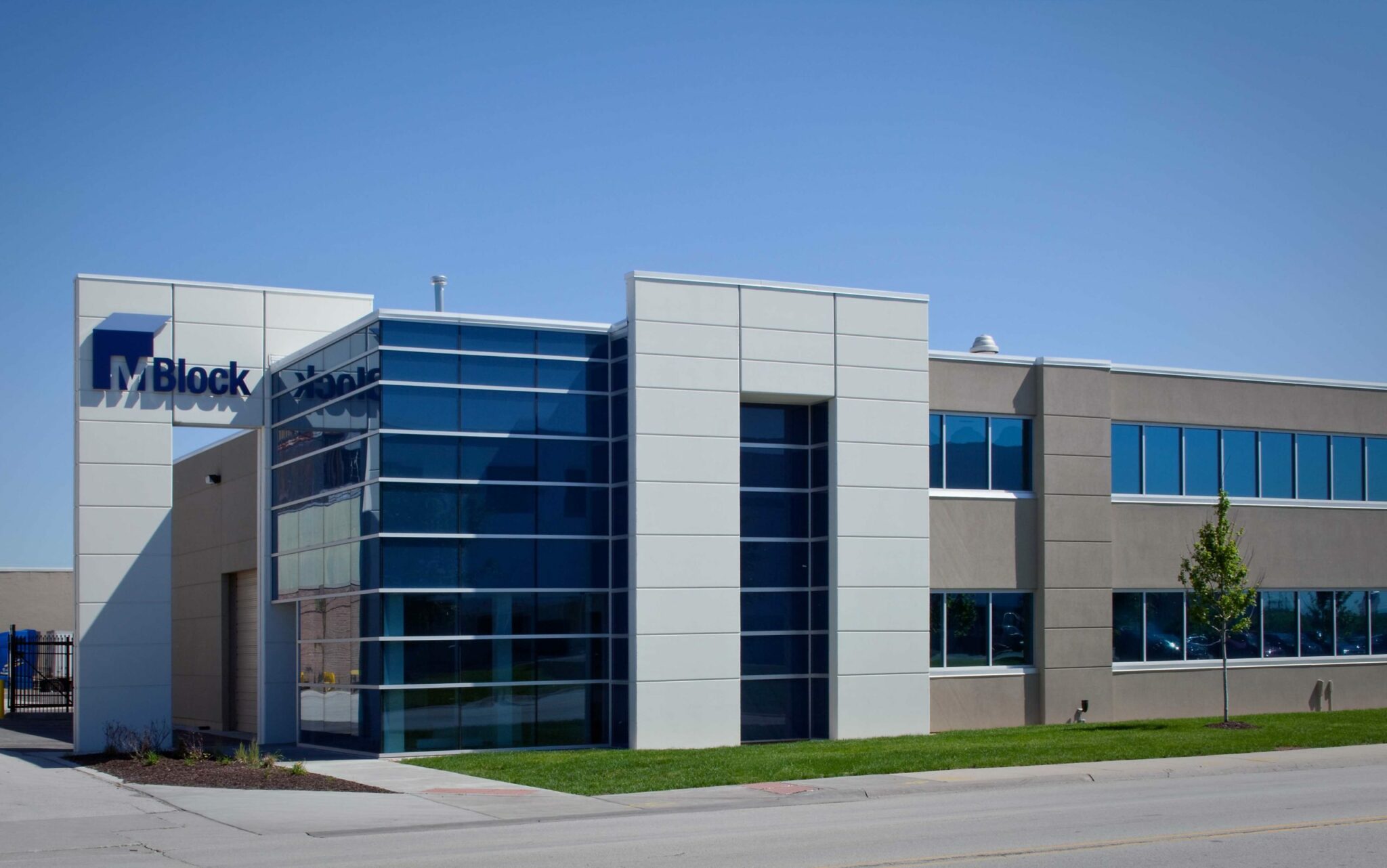 The mirrored windows at the front of the newly constructed M. Block and Sons’ corporate office and the warehouse area reflect the bright blue sky. The building has “M. Block” in large letters on a square sign with a sidewalk underneath it