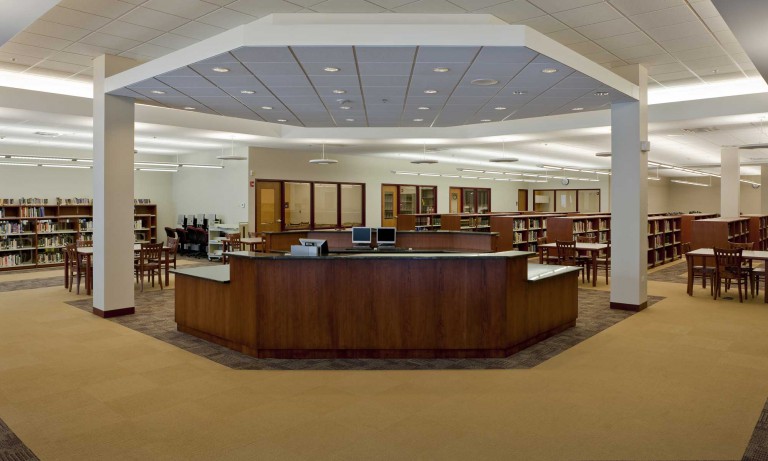 Montini Catholic High School’s library is an open-concept room with a prominent librarian’s desk, low bookshelves, a meeting room, and desks behind the welcome area.