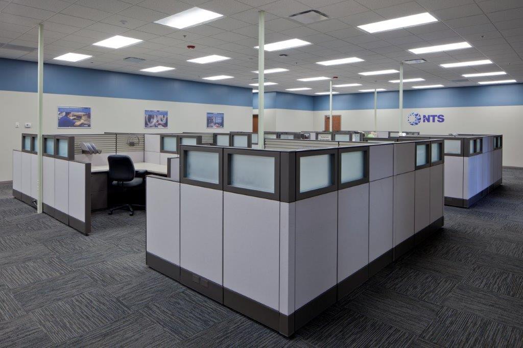 A brightly-lit, open-concept office space full of workspaces with short cubicle walls built for National Technical Systems by Keeley Construction, Inc.