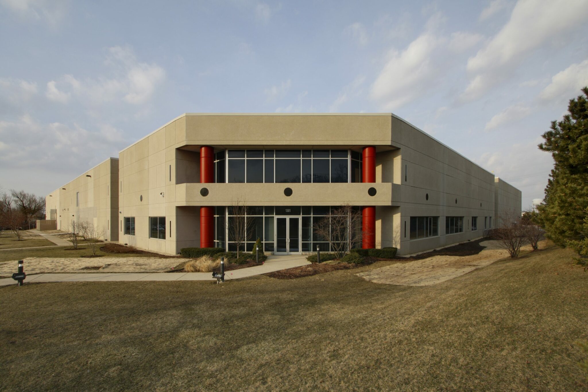 Two large red columns flank the flat corner entrance to the Ruprecht Meat Company Processing Facility. The large building stretches out behind the front doors to the left and right on a campus of manicured grass and trees.