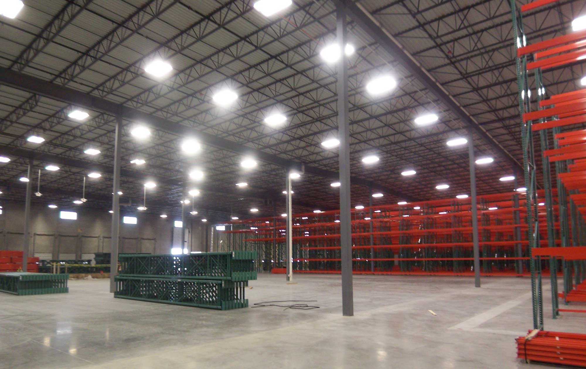 A well-lit new warehouse lined with tall metal racks with red shelves. Green pallets are on the floor.