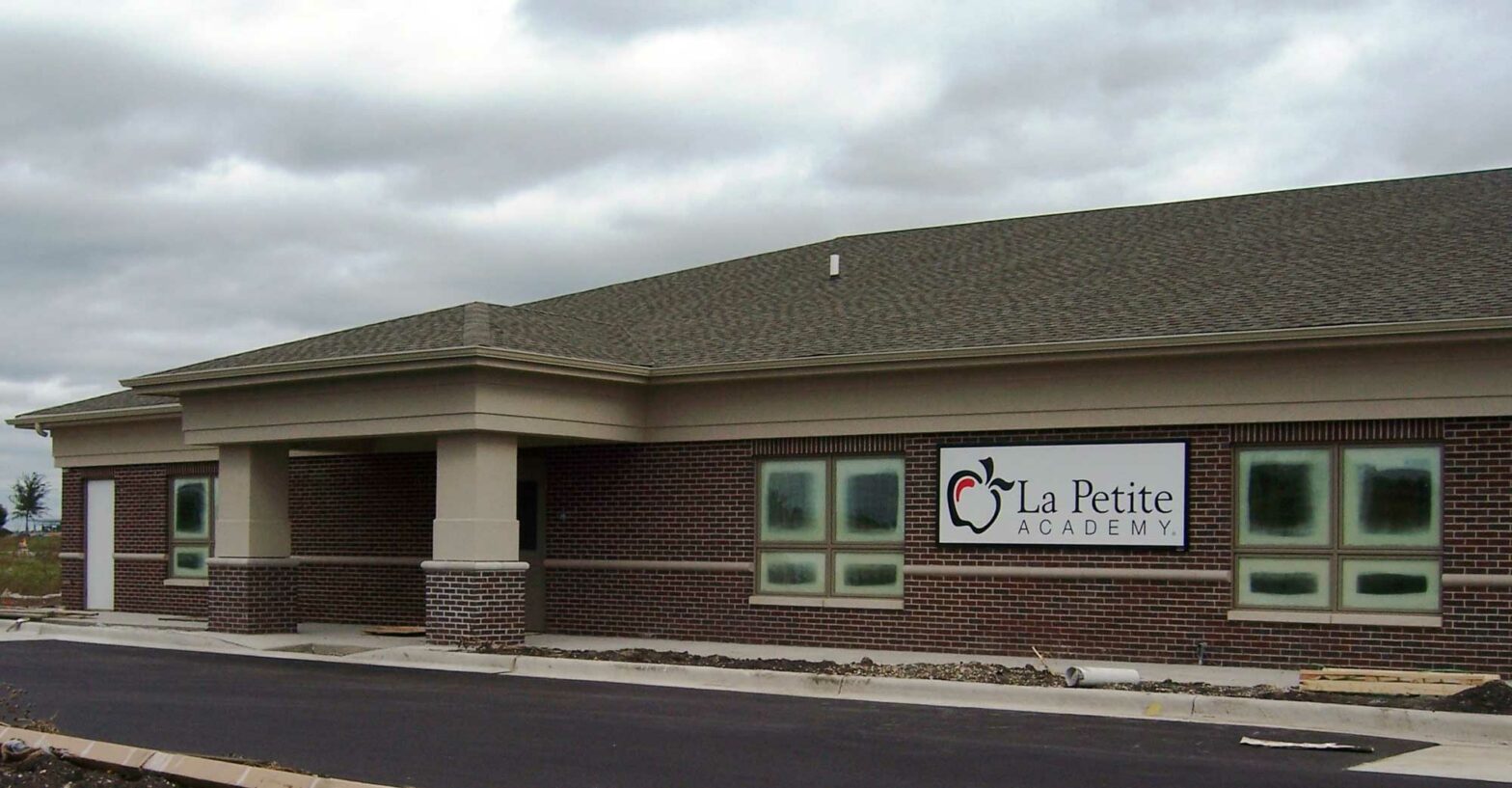 The outside of the single-story building is made of red bricks and stands against a grey sky. A white banner with an apple graphic says “La Petite Academy.” Keeley Construction, Inc. built the children’s daycare facility from the ground up.