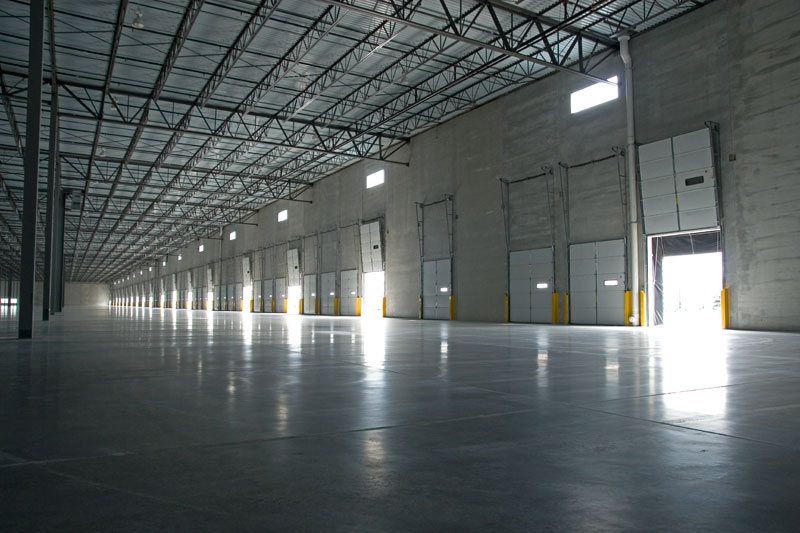 An angled view of a long shipping and receiving warehouse, with bay doors lining the far wall, letting in some natural light. This building and the nearly identical one next to it were part of the Keeley Construction East O’Hare Business Park project.