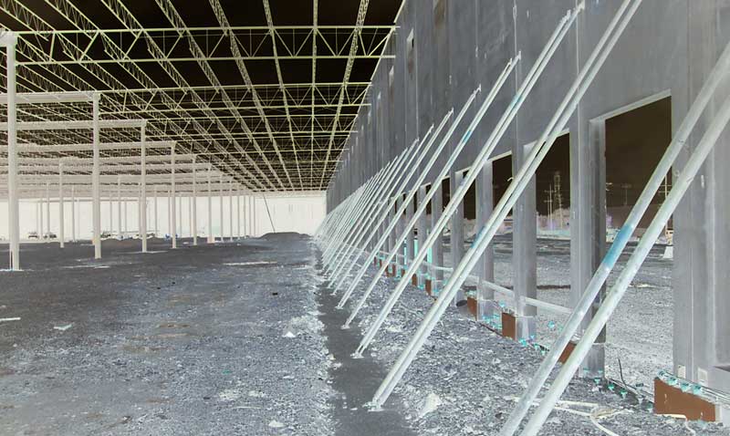 A view through a structure in progress in an outdoor space, with a low ceiling and metal struts supporting an unfinished wall, are all part of the new construction on the Toyota facility project completed by Keeley Construction, Inc.