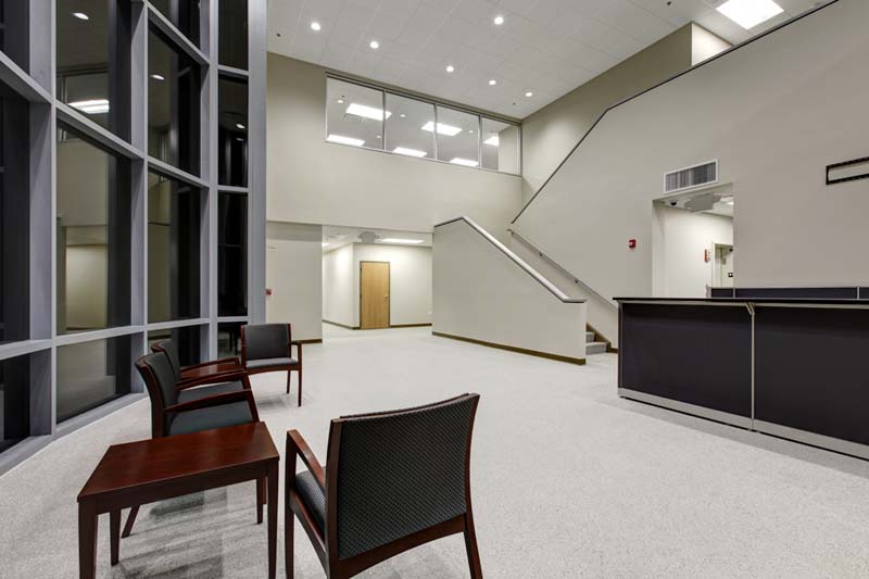 The lobby of the Wesco office building is full of light. The dark waiting chairs and reception desk contrast with the white walls, floor, and staircase.