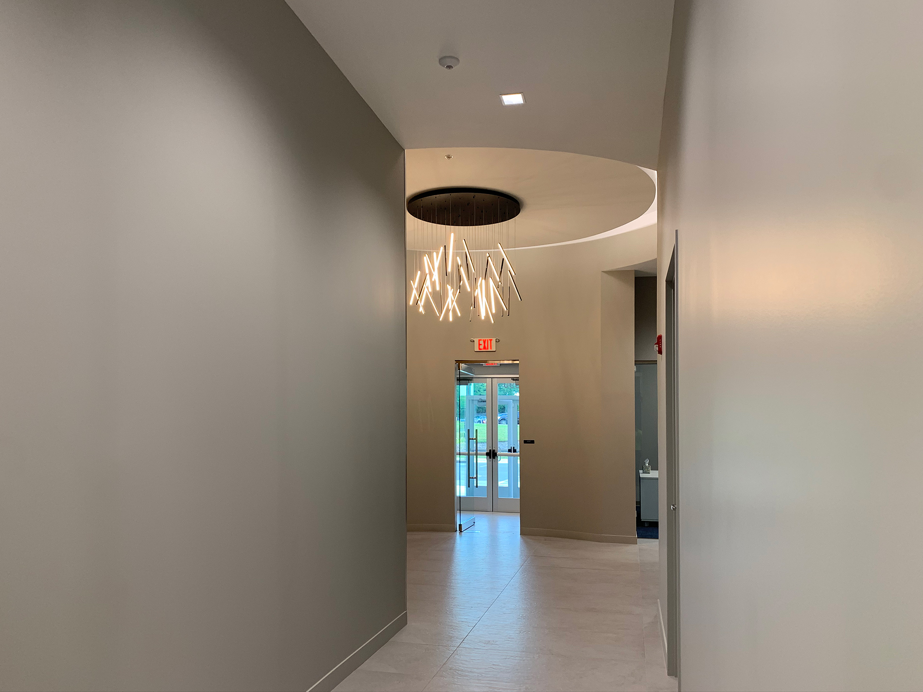 A modern glass chandelier is made of cylinders of lights and hangs in a round entryway at the end of a hall.