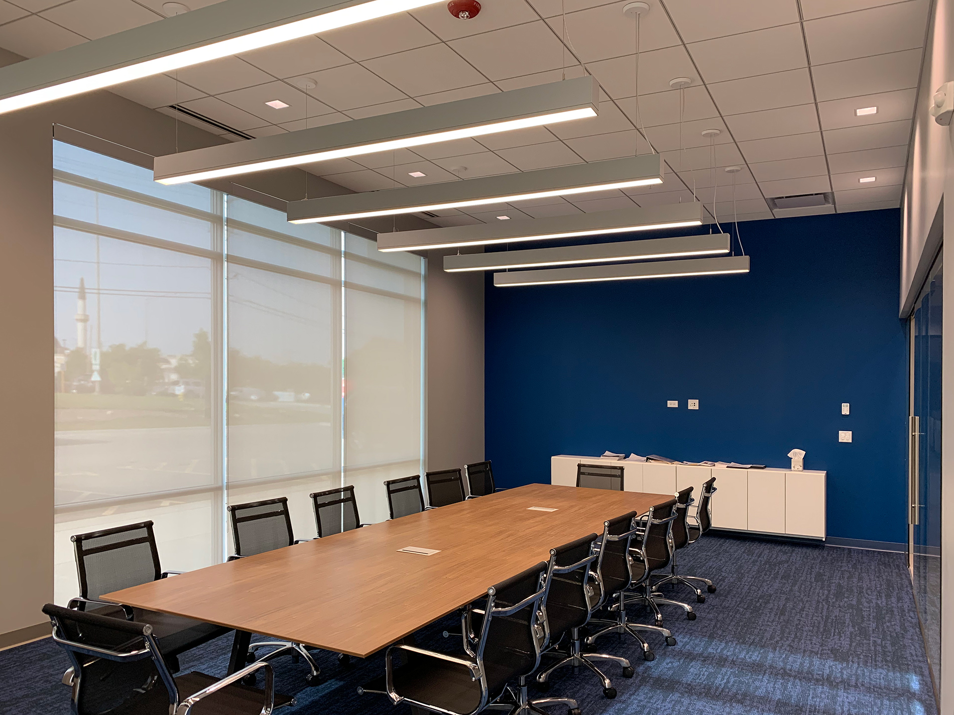 A large wall of windows take up one side of a conference room with a long table and a blue wall.