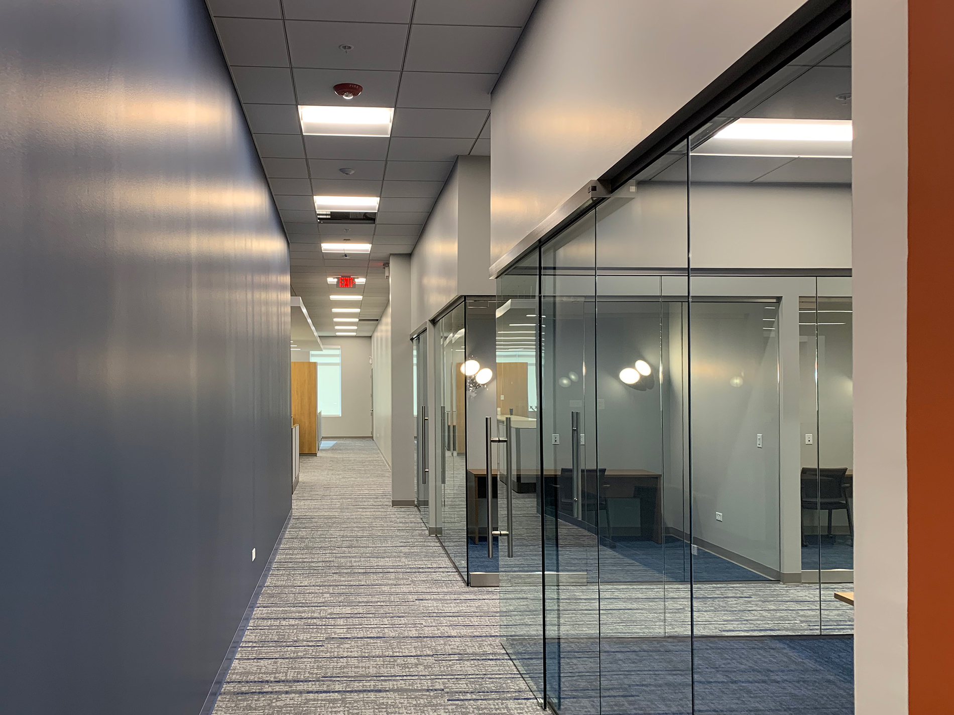 A long carpeted hallway in the renovated CODA building shows a solid wall on one side and offices with glass doors on the other side.