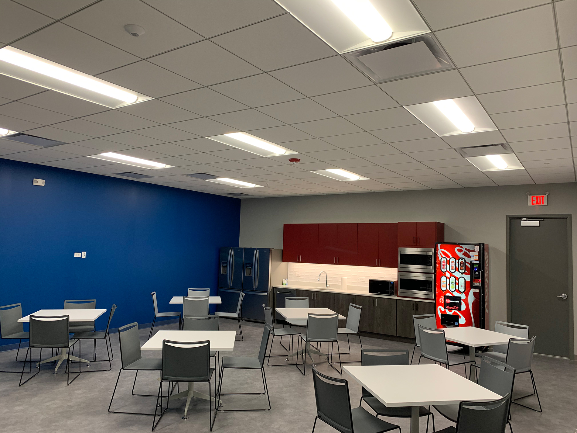 One of CODA’s employee lounges has square tables and chairs, a kitchenette and a vending machine. The wall on the left is blue.