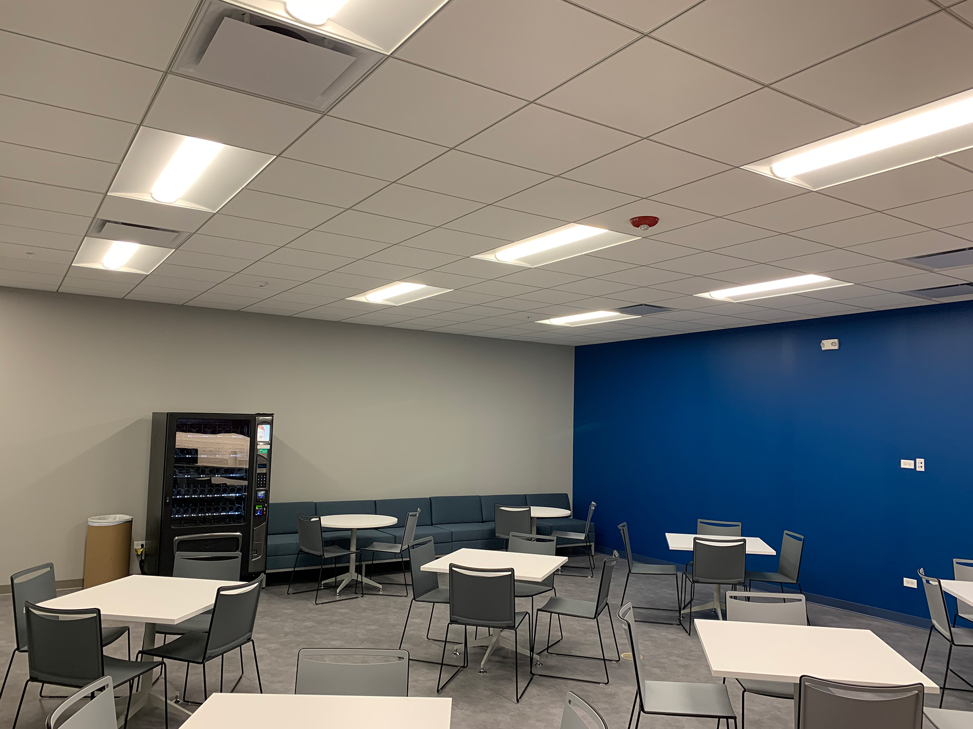 Square tables with four chairs each are in an empty CODA employee rest area. The back wall is blue.