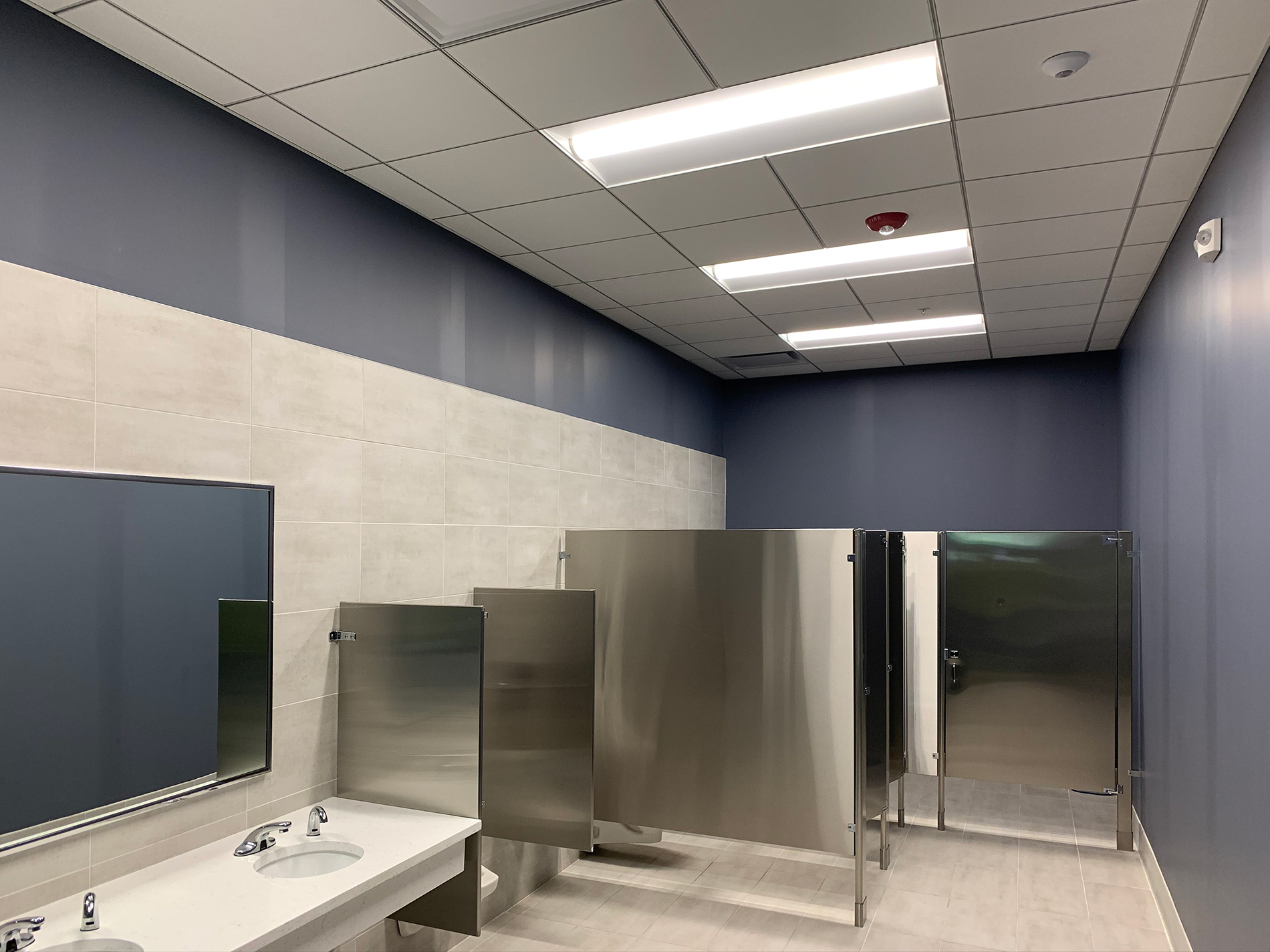 A long view of a new bathroom in CODA shows clean sinks and silver-colored stalls and partitions.