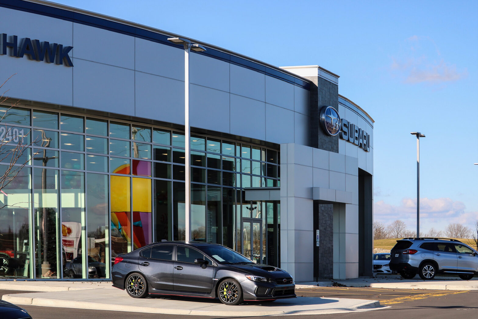 The entrance to the brand-new Hawk Auto is a rounded front with a black car outside the glass wall of the showroom.