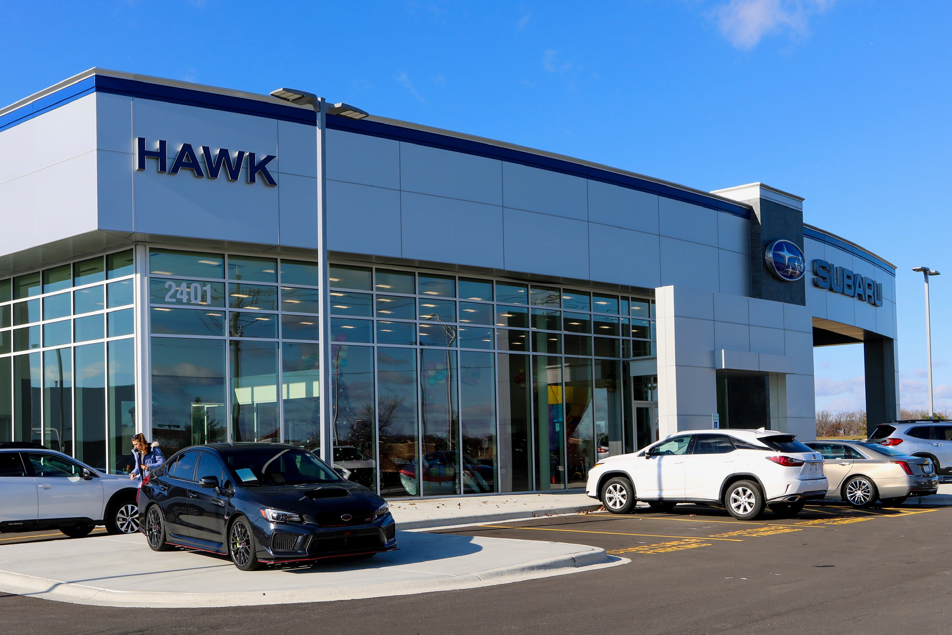 Black and white cars in the Hawk Auto parking lot in front of the entrance to the dealership.