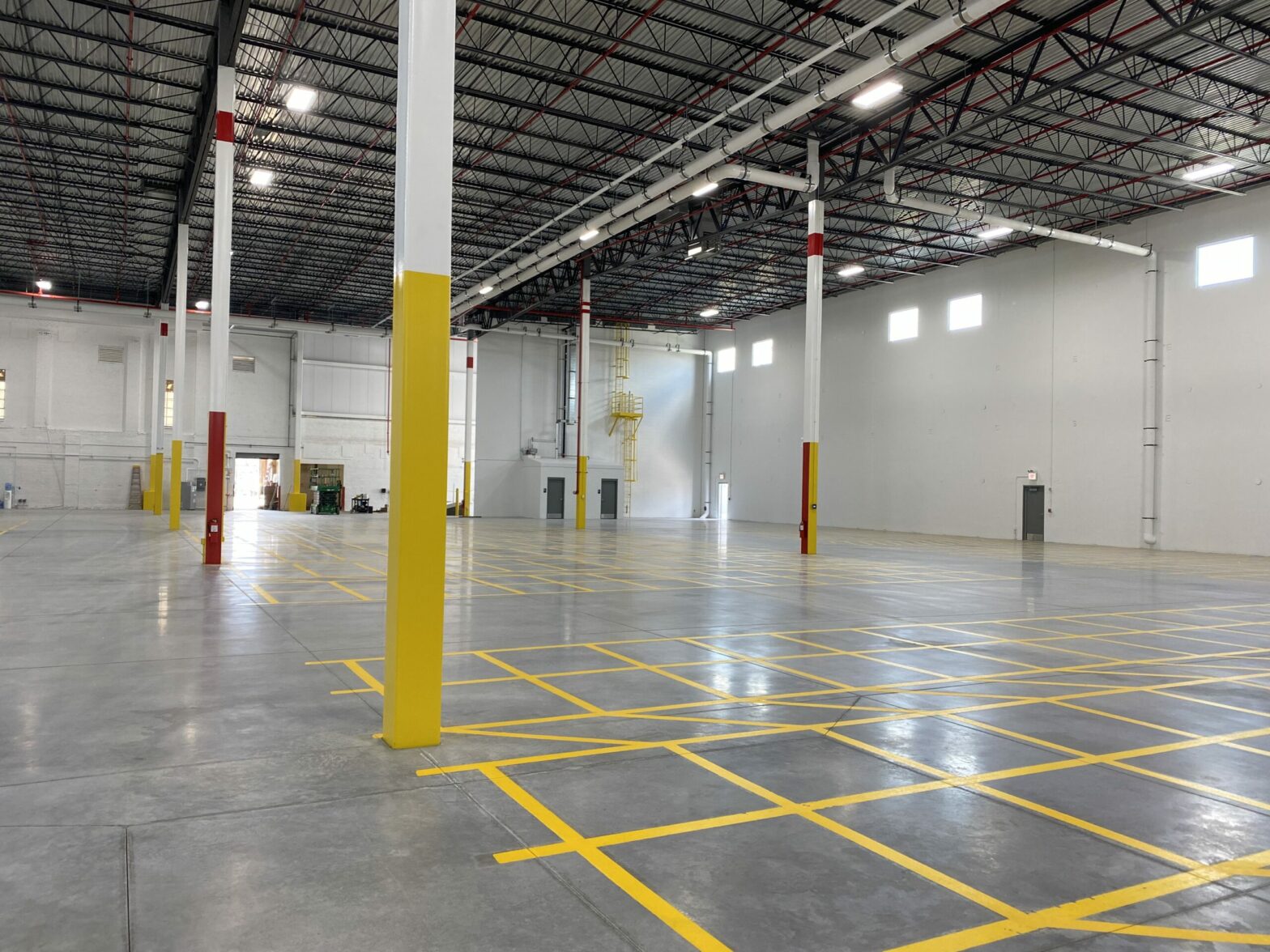 A large, empty, brand-new warehouse space for Nalco Chemical, with yellow paint marking important areas, an open bay door in the backroom, and the bright lights reflecting on the smooth floor.