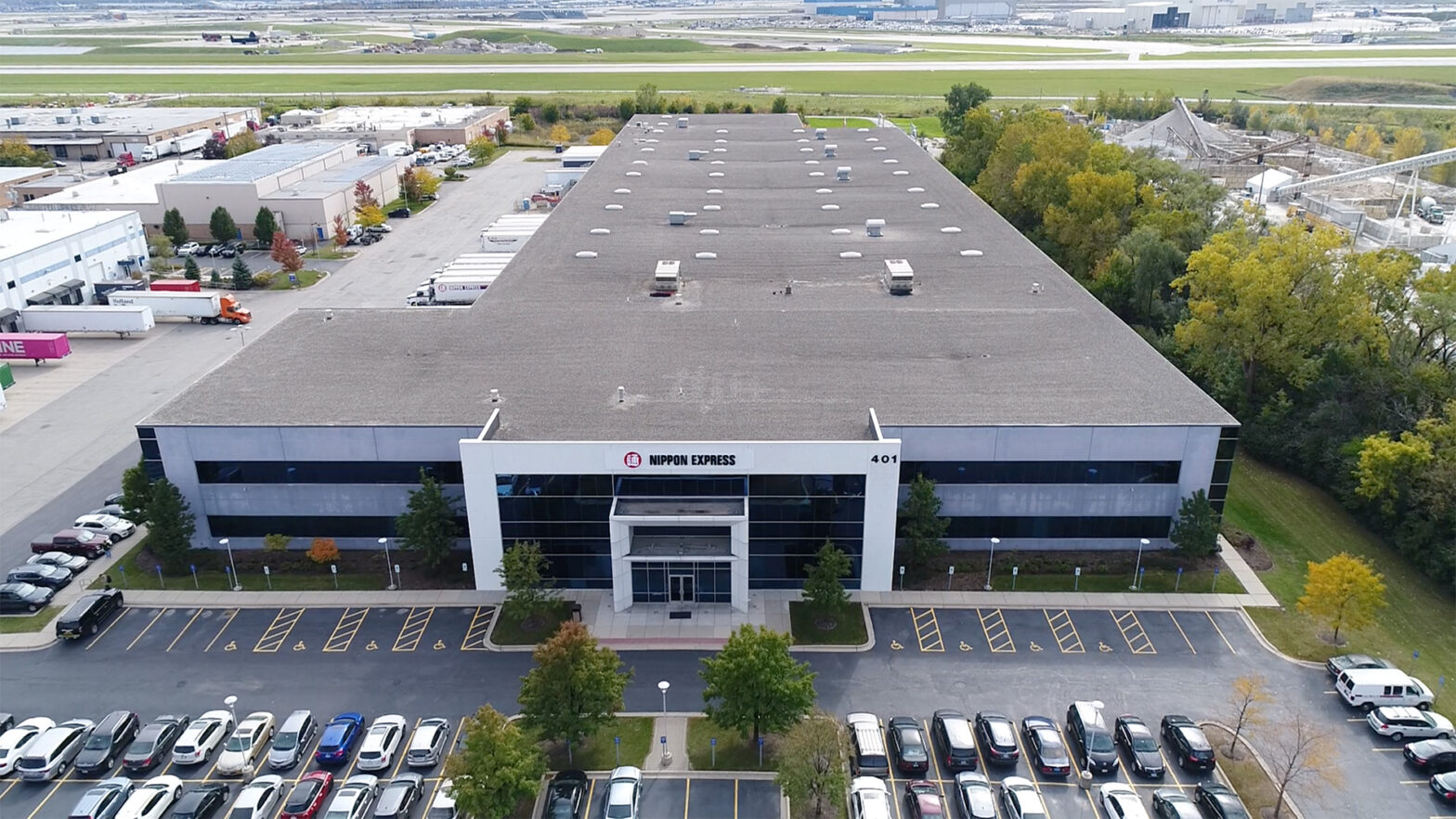 A close aerial view of Nippon Express shows their long, recently renovated building and a parking lot in front.