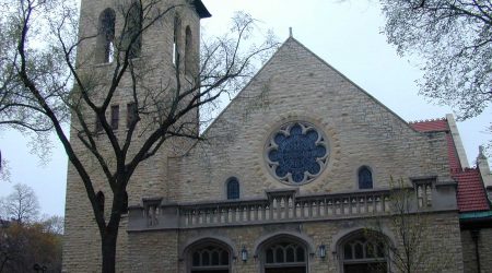 The exterior of First Presbyterian Church shows a brick and stone exterior with a bell tower hidden behind a winter tree.