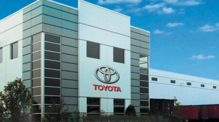 The front of a large office building and warehouse pictured on a bright sunny day is inviting. The words “Toyota” and the Toyota logo hang off the building’s top floor.