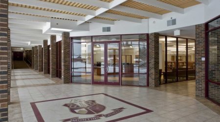 Montini Catholic High School’s front entrance has red brick walls and the school’s red crest on the tiled floor, creating a warm and professional impression built by Keeley Construction.