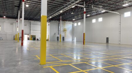 A large, empty, brand-new warehouse space for Nalco Chemical, with yellow paint marking important areas, an open bay door in the backroom, and the bright lights reflecting on the smooth floor.