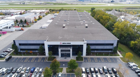 A close aerial view of Nippon Express shows their long, recently renovated building and a parking lot in front.