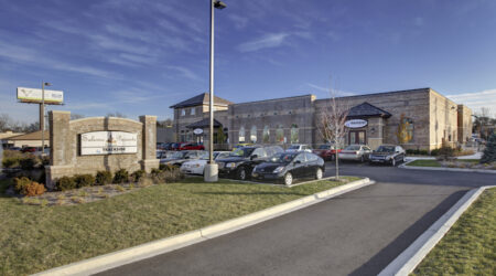 A comforting light brick building behind a nice parking lot and a brick sign that reads, "Trackside."