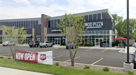 A parking lot is seen in front of a large building with many windows. The sign on the nearest corner reads “T-Moble.” The Shoppes at Buffalo Grove offer multiple retail spaces.