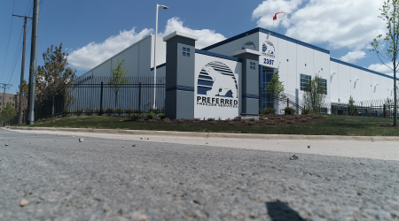 The outside of the Preferred Freezer Services building has a black fence and a large sign with the company’s logo, a white polar bear viewed from the side, and the text “Preferred Freezer Services” below the bear. The logo is repeated in a smaller version on the top of the building’s side, above the address text “2357.”