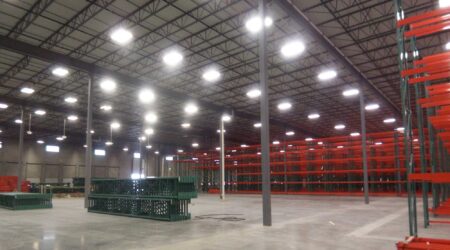 A well-lit new warehouse lined with tall metal racks with red shelves. Green pallets are on the floor.