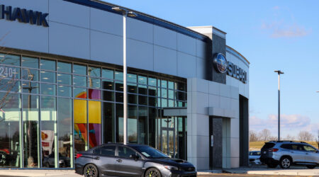 The entrance to the brand-new Hawk Auto is a rounded front with a black car outside the glass wall of the showroom.