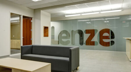 A reception area contains a couch and a desk in front of a frosted glass wall. The word “Lenze” in large letters is not frosted and easily readable.