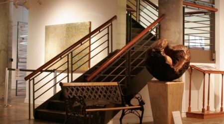 A wooden park bench sits next to a large circular structure placed to the side of the metal staircase in the lower level gallery space in the National Vietnam Veterans Art Museum. Keeley Construction was instrumental in renovating the 80-year-old damaged building.