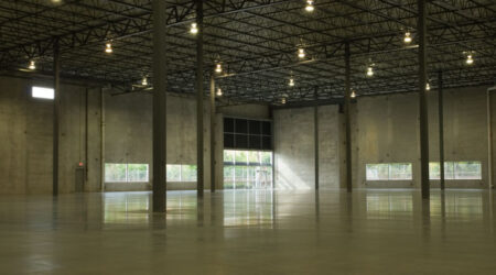 An empty, low-lit concrete warehouse has a couple of support columns and a large rectangular window in the concrete walls. This building is one of two nearly identical facilities built by Keeley Construction in the O'Hare East Business Park.