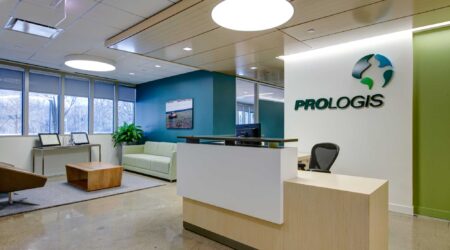 An interior reception area with the words "Prologis” below a swirled logo on the wall shows modern furnishings and fresh blue walls. This O'Hare Industrial Park Façade Renovation by Keeley Construction is a sustainability LEED Gold project.